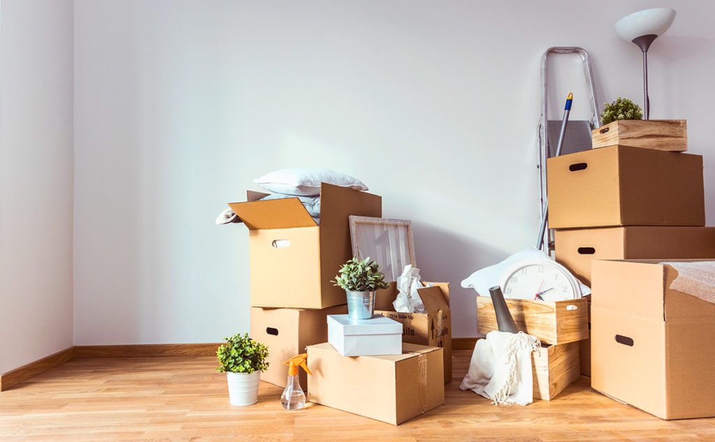 Stacks of boxes and miscellaneous items in an empty apartment with wood floors and white walls