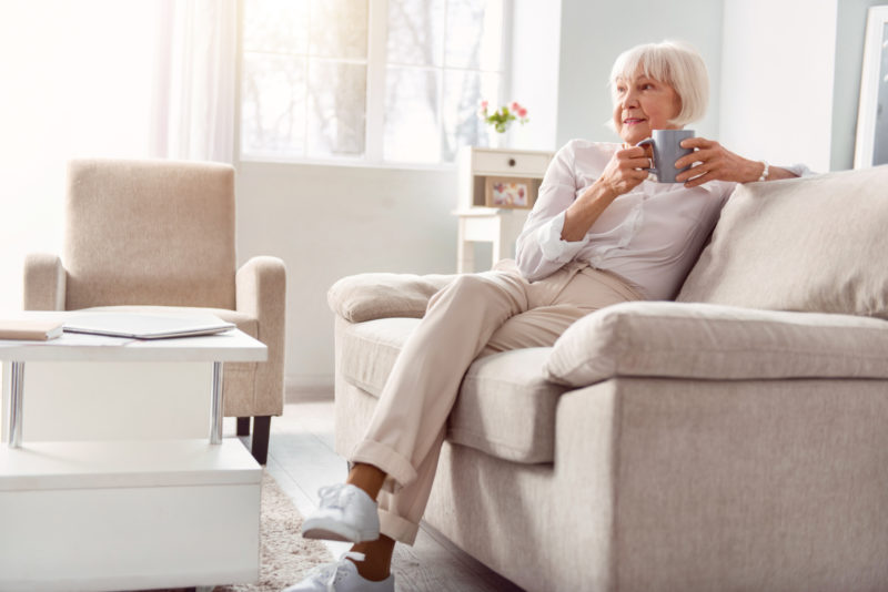 Elderly Woman sitting on ottoman drinking coffee