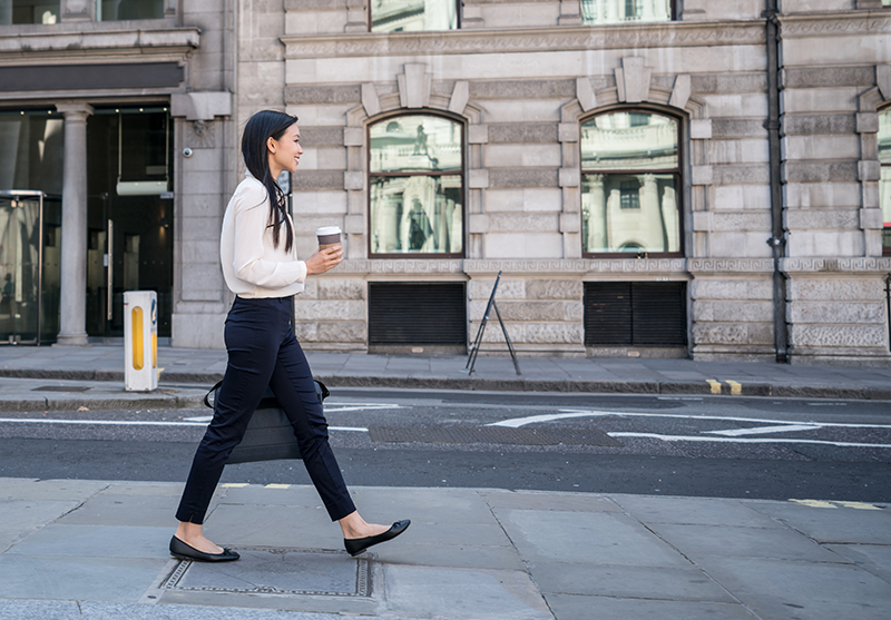 Happy young female in business attire walking on the sidewalk in the city