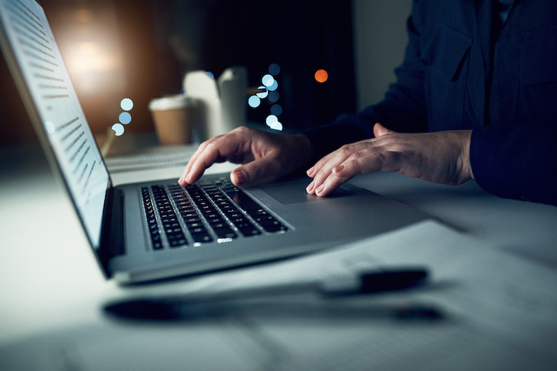 Hands on keyboard and mouse pad of laptop in dimly lit room