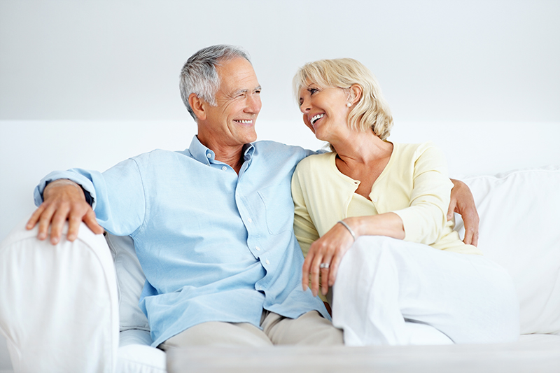Elderly couple smiling alongside one another on a white couch