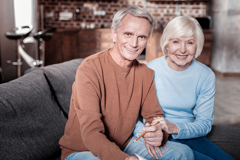 Elderly couple smiling at the camera while sitting on a couch