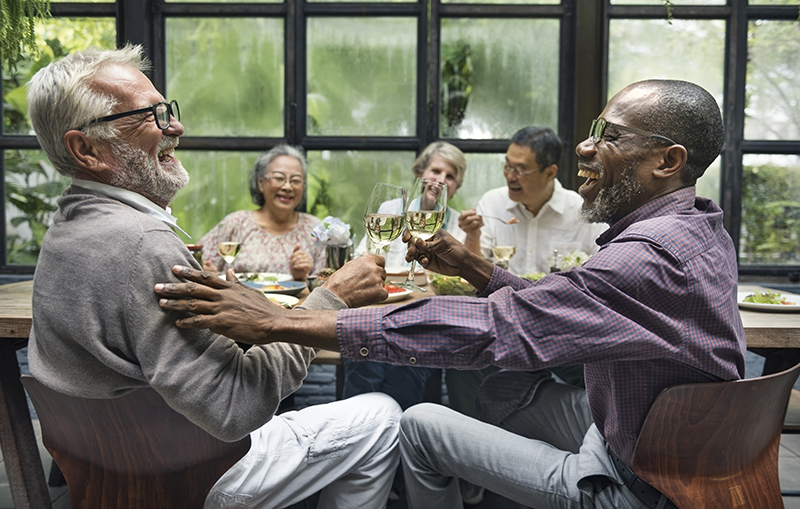 Elderly men and women laughing over white wine and dinner
