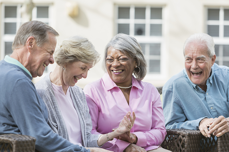 Elderly men and women sitting outside and laughing alongside one another