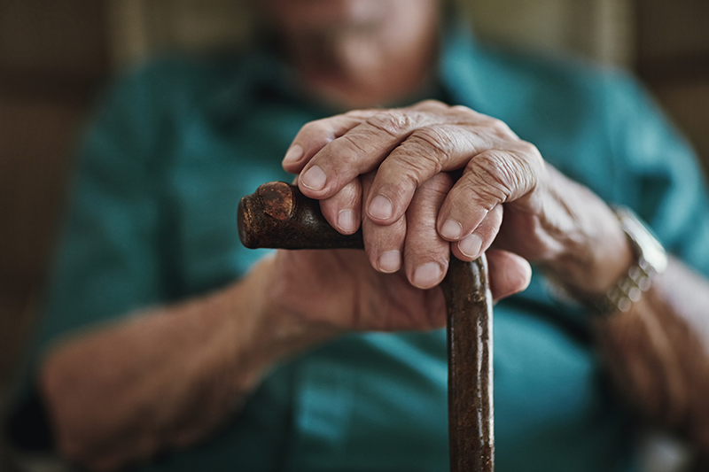 Elderly hands holding onto a cane with elderly man blurred out in the background