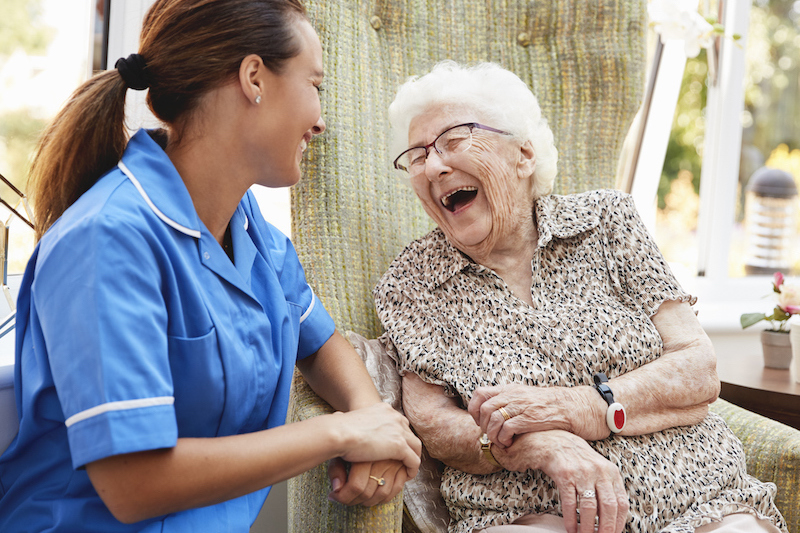 Young female nurse laughing alongside a joyous elderly woman dressed in vibrant cheetah print shirt