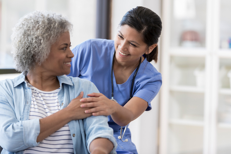 Young nurse and elderly woman holding hands and smiling at one another