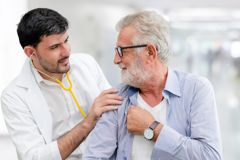 Youthful male doctor with stethoscope showing support to a sharp-dressed elderly man by putting his hand on his shoulder