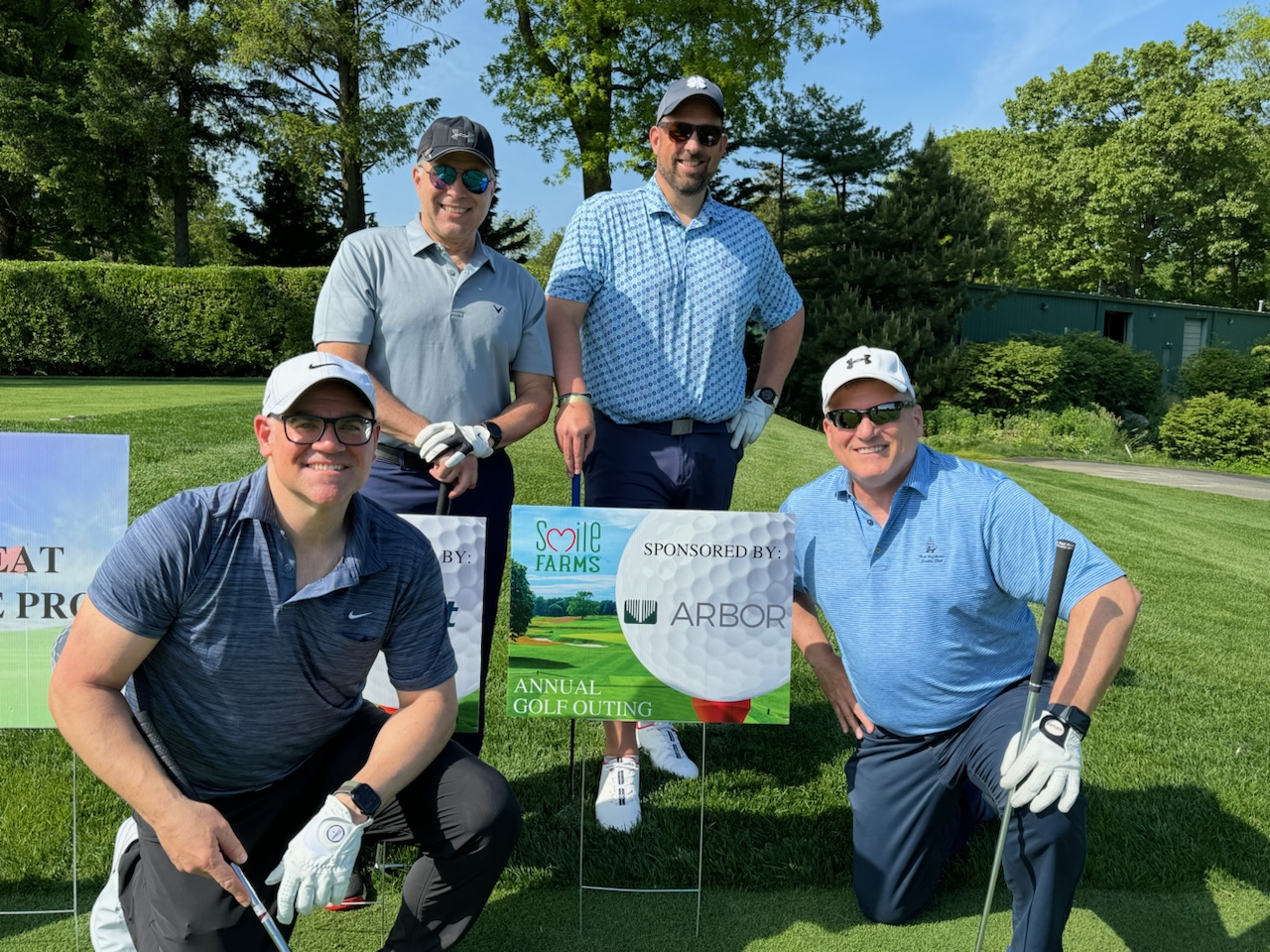 Four Arbor employees pose around a sponsorship sign on a golf course at the Smile Farms Golf Outing.