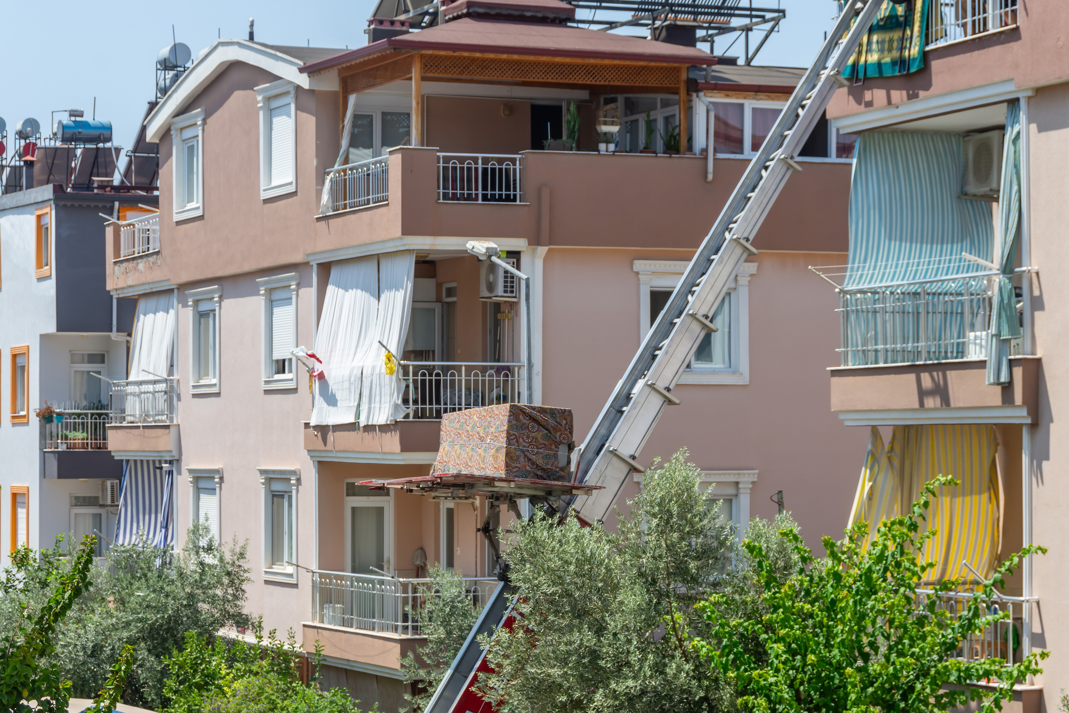 A box is moved up a ladder on a multifamily building undergoing renovations.
